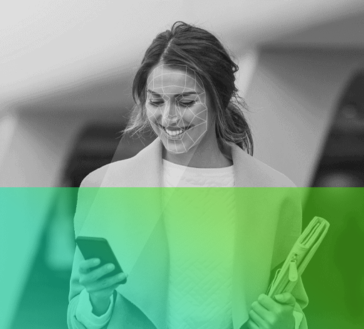 woman walking holding smart phone in right hand and computer in left hand. Woman has her hair up and is smiling at the phone. Phone is displaying biometric lines on face.