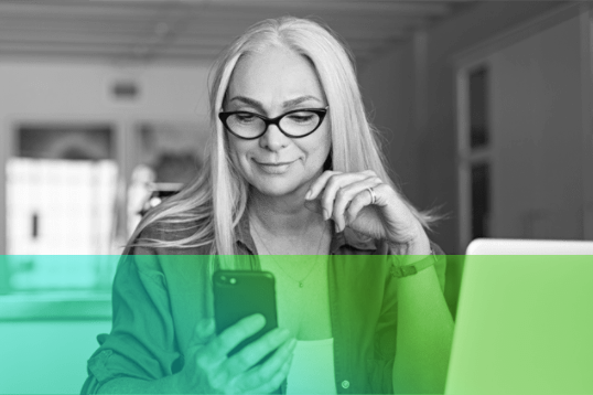 image of older female holding phone in her hand. Female is wearing glasses and has long blonde hair.